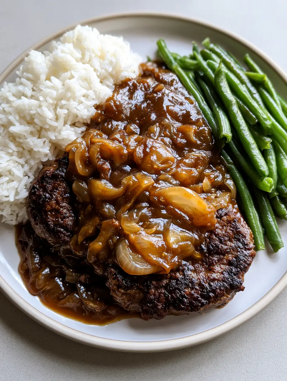 A white plate featuring two charred ground beef patties covered in dark brown gravy with onions, served with white rice and green beans. (Hamburger Steak with Brown Gravy)
