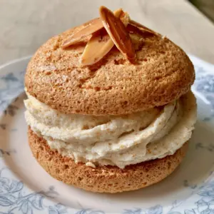 Single handheld Almond Dacquoise Cookie showing the porous texture of the golden-brown meringue and smooth ivory cream.