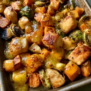 Close up top-down view of roasted chicken breast chunks and caramelized sweet potatoes with visible mustard seeds. (Sheet Pan Honey Dijon Chicken)